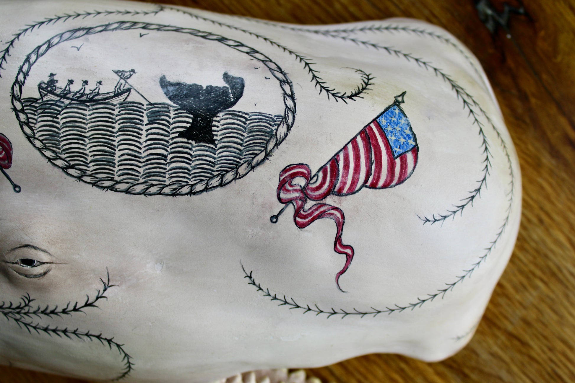 Hanging sperm whale sculpture by Laura Rotelli.  Sperm whale porcelain sculpture with scrimshaw designs of whaling scenes and ships painted on the surface.  Maritime art, marine art, folk art, Americana, patriotic art