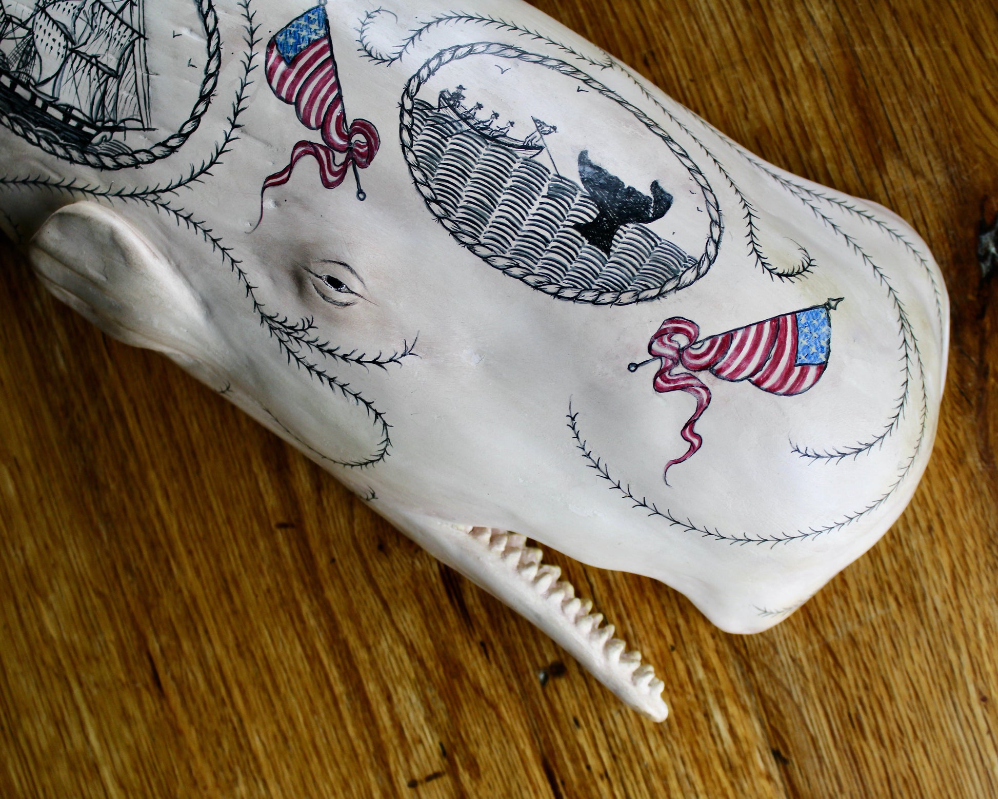 Hanging sperm whale sculpture by Laura Rotelli.  Sperm whale porcelain sculpture with scrimshaw designs of whaling scenes and ships painted on the surface.  Maritime art, marine art, folk art, Americana, patriotic art