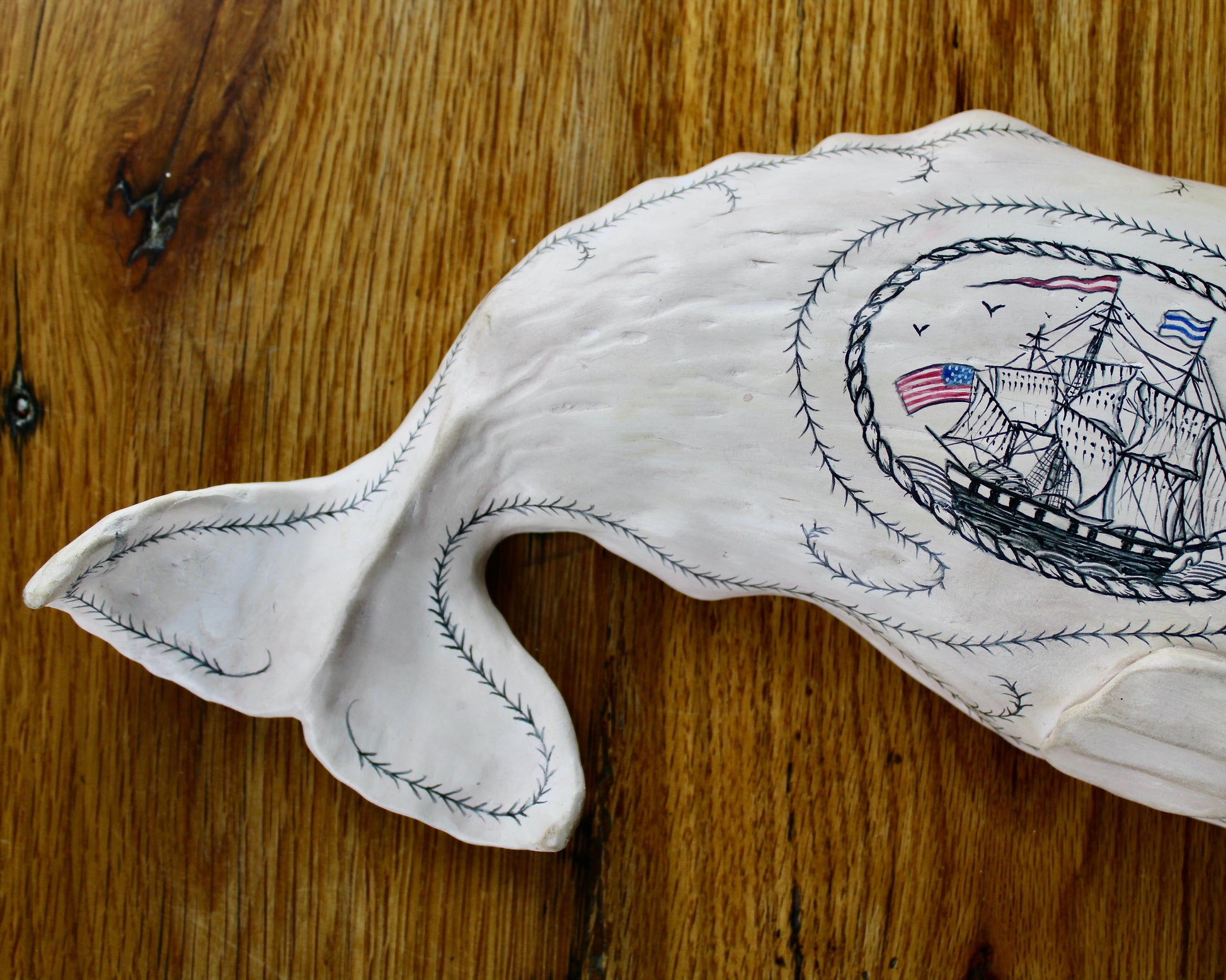 Hanging sperm whale sculpture by Laura Rotelli.  Sperm whale porcelain sculpture with scrimshaw designs of whaling scenes and ships painted on the surface.  Maritime art, marine art, folk art, Americana, patriotic art