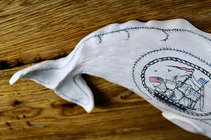 Hanging sperm whale sculpture by Laura Rotelli.  Sperm whale porcelain sculpture with scrimshaw designs of whaling scenes and ships painted on the surface.  Maritime art, marine art, folk art, Americana, patriotic art