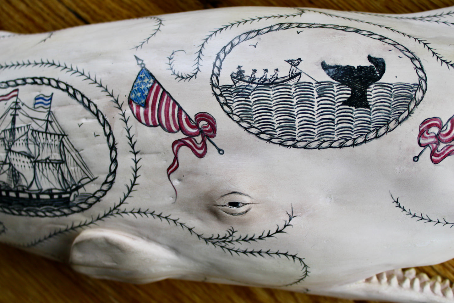 Hanging sperm whale sculpture by Laura Rotelli.  Sperm whale porcelain sculpture with scrimshaw designs of whaling scenes and ships painted on the surface.  Maritime art, marine art, folk art, Americana, patriotic art