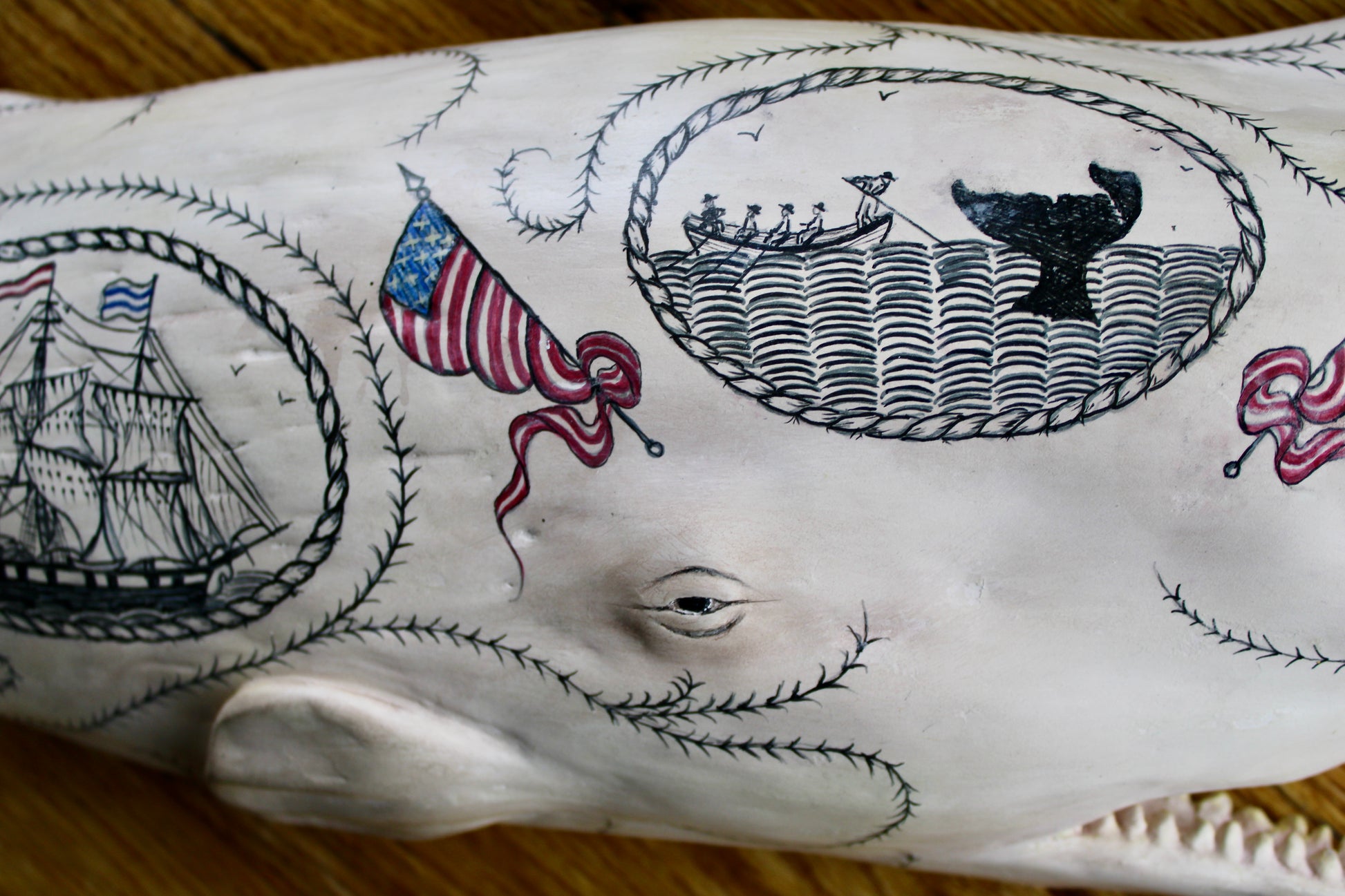 Hanging sperm whale sculpture by Laura Rotelli.  Sperm whale porcelain sculpture with scrimshaw designs of whaling scenes and ships painted on the surface.  Maritime art, marine art, folk art, Americana, patriotic art