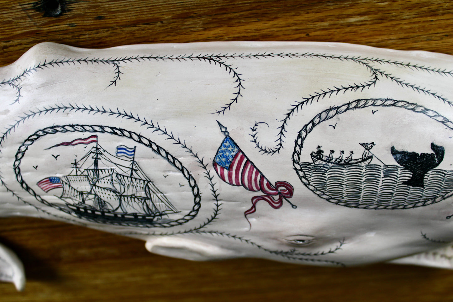 Hanging sperm whale sculpture by Laura Rotelli.  Sperm whale porcelain sculpture with scrimshaw designs of whaling scenes and ships painted on the surface.  Maritime art, marine art, folk art, Americana, patriotic art