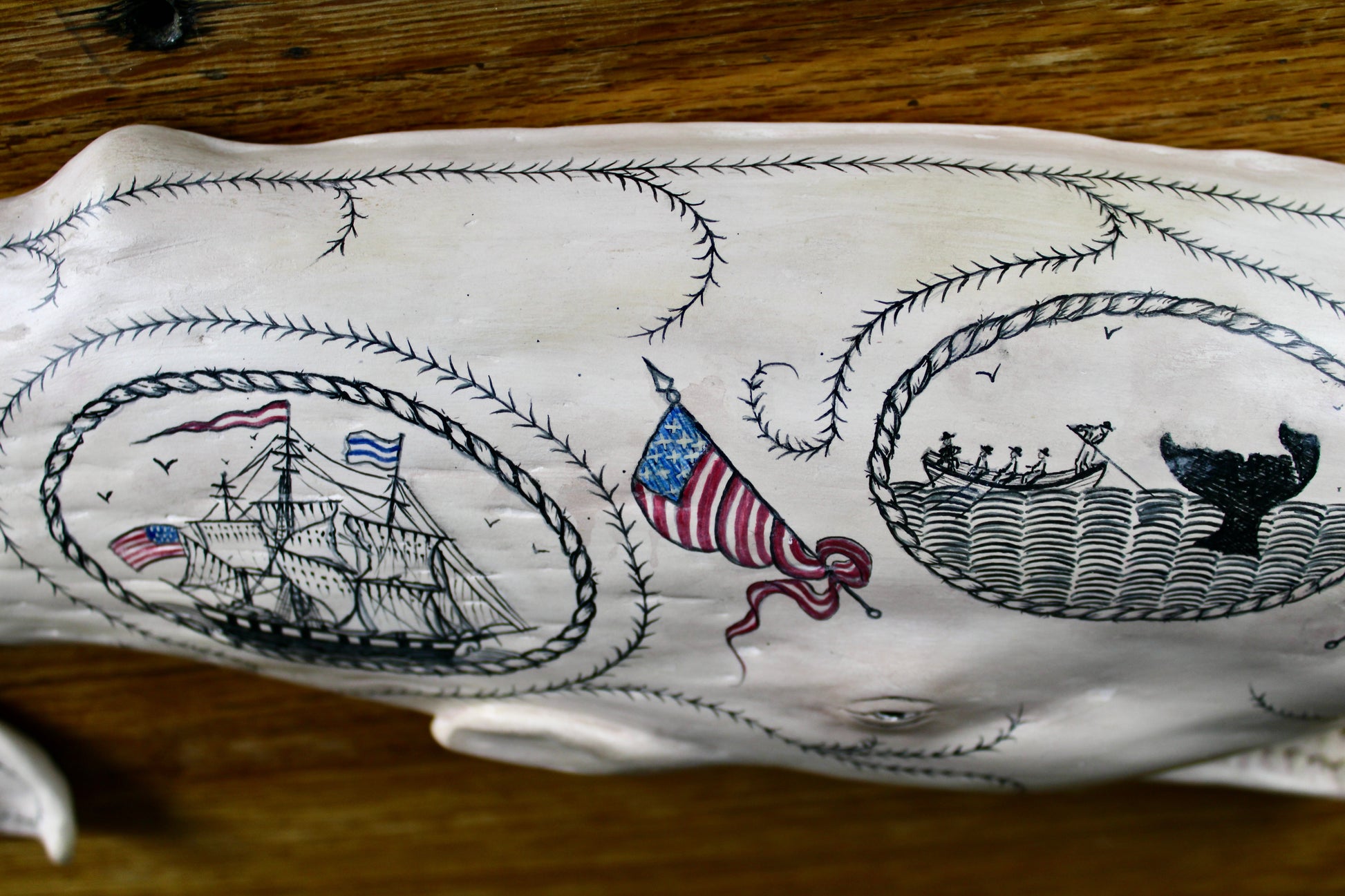Hanging sperm whale sculpture by Laura Rotelli.  Sperm whale porcelain sculpture with scrimshaw designs of whaling scenes and ships painted on the surface.  Maritime art, marine art, folk art, Americana, patriotic art