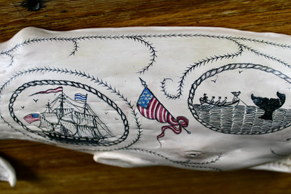 Hanging sperm whale sculpture by Laura Rotelli.  Sperm whale porcelain sculpture with scrimshaw designs of whaling scenes and ships painted on the surface.  Maritime art, marine art, folk art, Americana, patriotic art