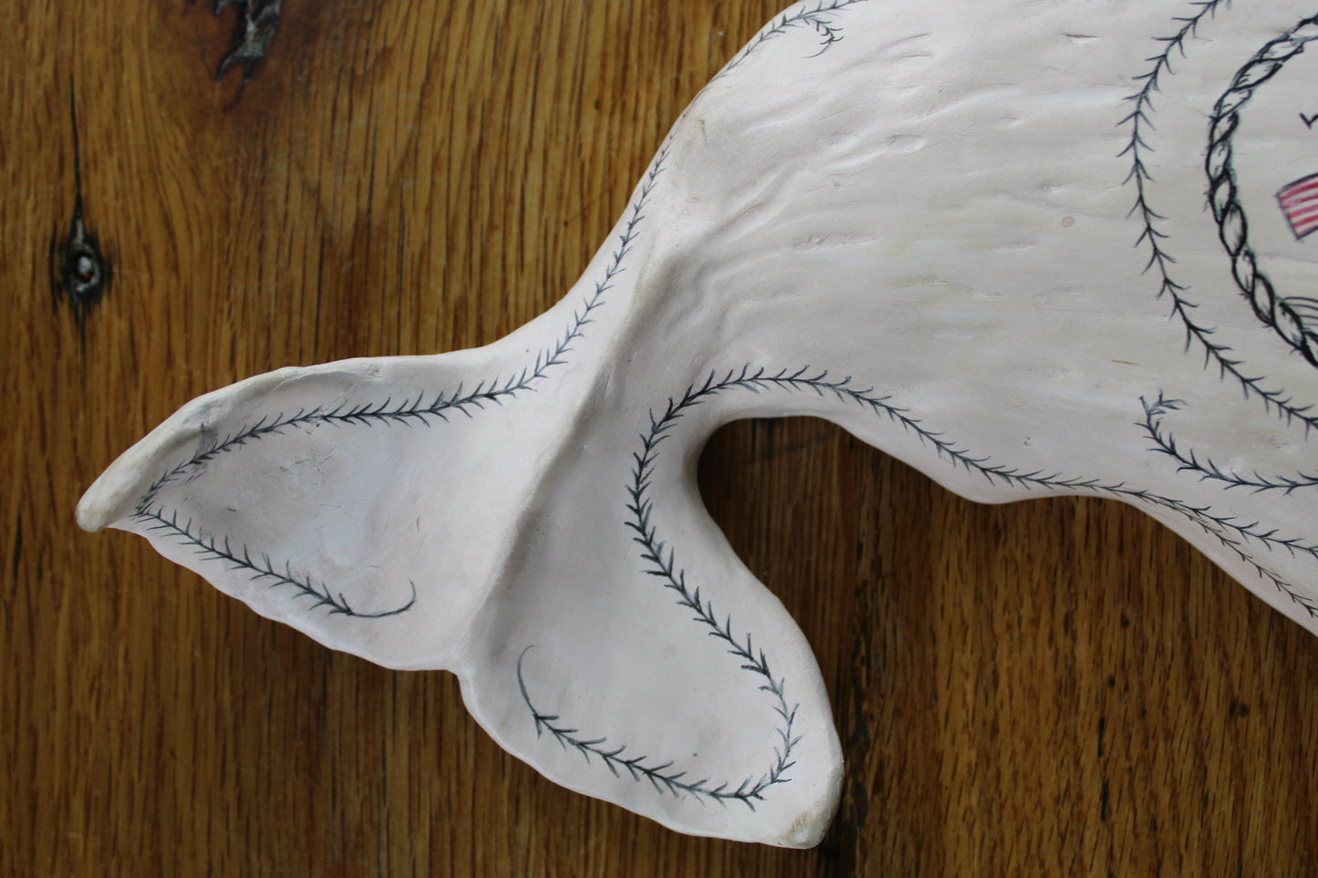 Hanging sperm whale sculpture by Laura Rotelli.  Sperm whale porcelain sculpture with scrimshaw designs of whaling scenes and ships painted on the surface.  Maritime art, marine art, folk art, Americana, patriotic art