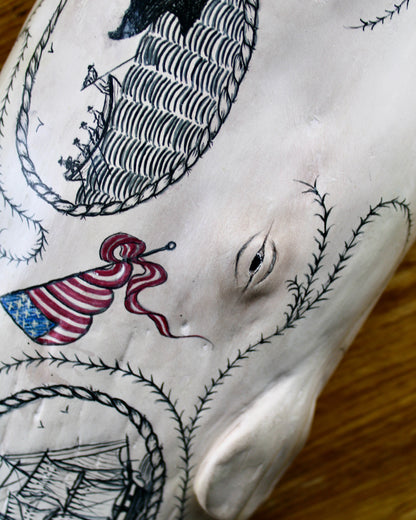 Hanging sperm whale sculpture by Laura Rotelli.  Sperm whale porcelain sculpture with scrimshaw designs of whaling scenes and ships painted on the surface.  Maritime art, marine art, folk art, Americana, patriotic art