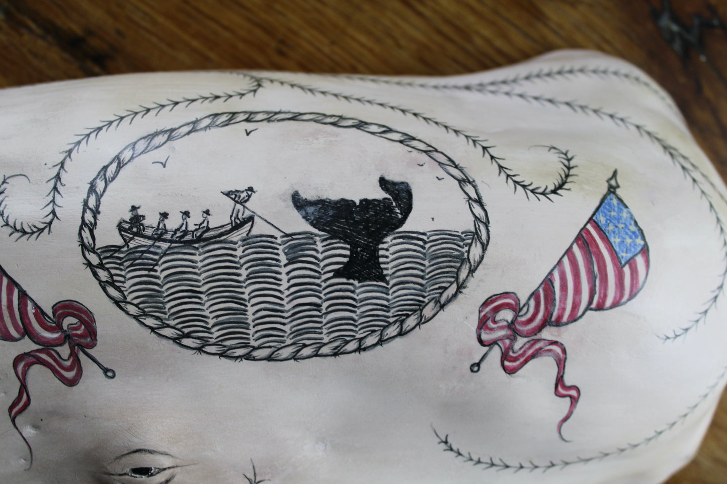 Hanging sperm whale sculpture by Laura Rotelli.  Sperm whale porcelain sculpture with scrimshaw designs of whaling scenes and ships painted on the surface.  Maritime art, marine art, folk art, Americana, patriotic art