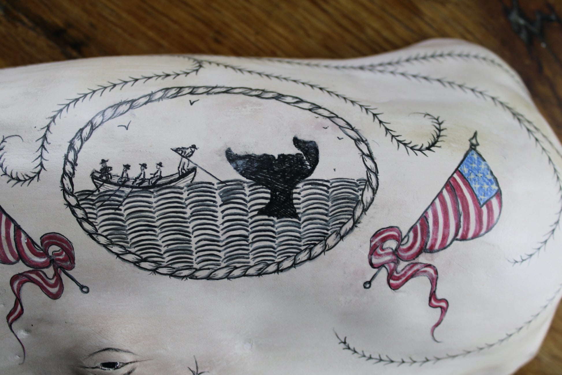 Hanging sperm whale sculpture by Laura Rotelli.  Sperm whale porcelain sculpture with scrimshaw designs of whaling scenes and ships painted on the surface.  Maritime art, marine art, folk art, Americana, patriotic art