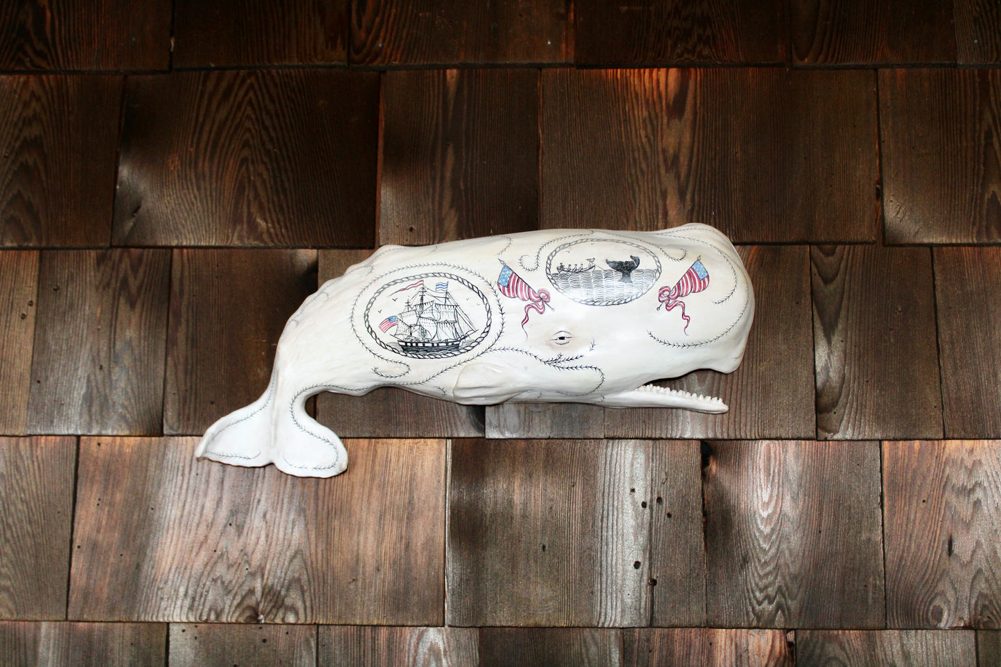 Hanging sperm whale sculpture by Laura Rotelli.  Sperm whale porcelain sculpture with scrimshaw designs of whaling scenes and ships painted on the surface.  Maritime art, marine art, folk art, Americana, patriotic art
