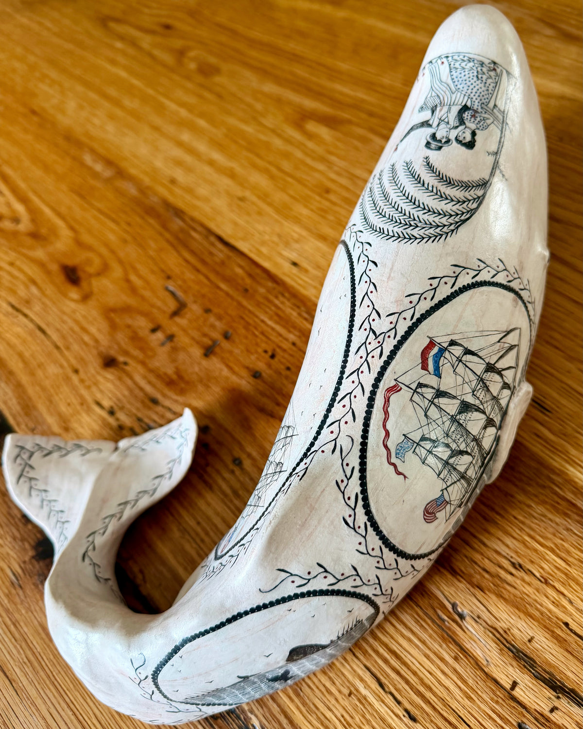 American contemporary folk art by Laura Rotelli.   Porcelain sperm whale sculpture with painted scrimshaw designs of sailing ships and whaling scenes, coastal maritime nautical artwork.