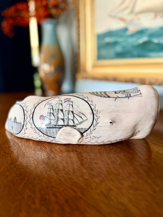 Edward II porcelain sperm whale sculpture with black scrimshaw-style ships, displayed beneath a maritime painting. American contemporary folk art by Laura Rotelli.   Porcelain sperm whale sculpture with painted scrimshaw designs of sailing ships and whaling scenes, coastal maritime nautical artwork