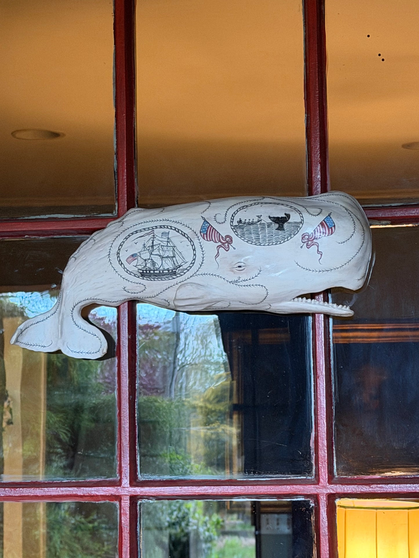 Hanging sperm whale sculpture by Laura Rotelli.  Sperm whale porcelain sculpture with scrimshaw designs of whaling scenes and ships painted on the surface.  Maritime art, marine art, folk art, Americana, patriotic art