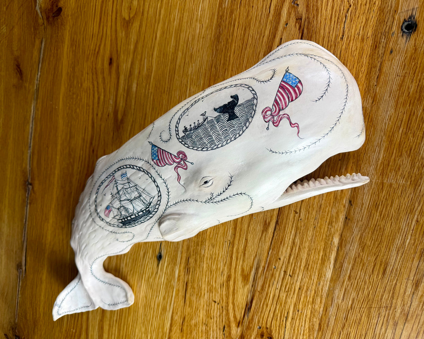 Hanging sperm whale sculpture by Laura Rotelli.  Sperm whale porcelain sculpture with scrimshaw designs of whaling scenes and ships painted on the surface.  Maritime art, marine art, folk art, Americana, patriotic art